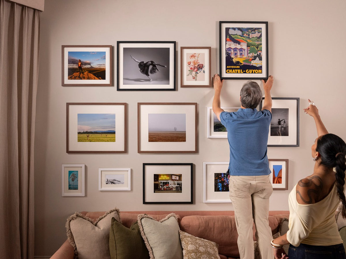 A couple hanging a gallery wall above their sofa