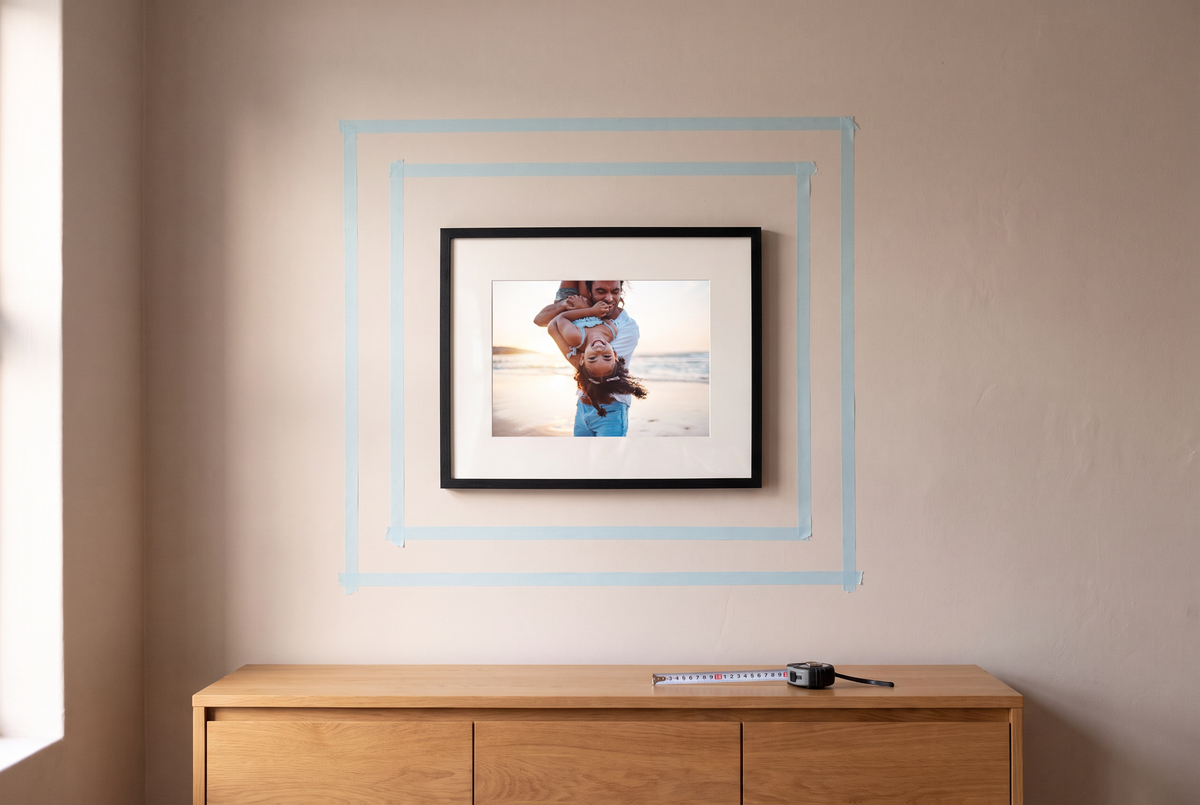 A black Framewick frame on a plain wall with masking tape rectangles marking out two larger frame sizes around it